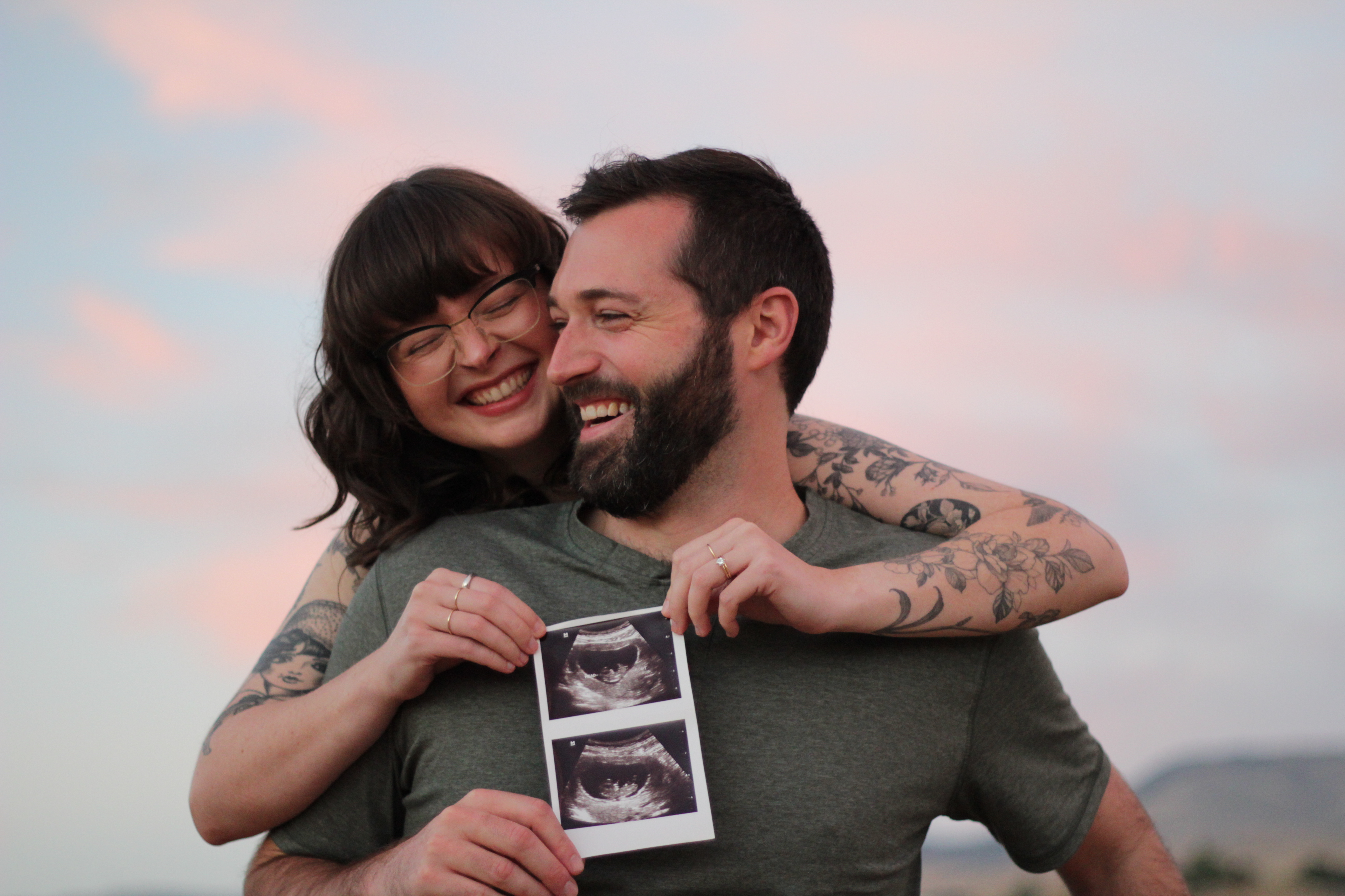 Happy couple holding ultrasound photos, sunset sky